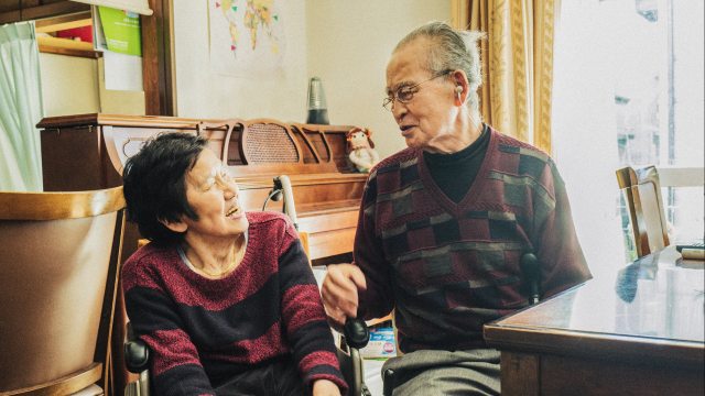 Woman in wheelchair smiles at older man sitting by a table